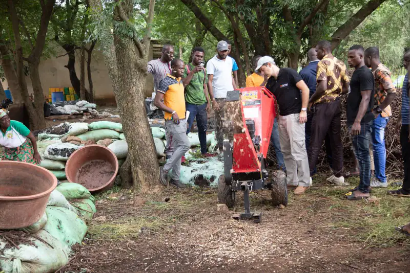 Trainees gather round a compost shredder during a practical session outdoors