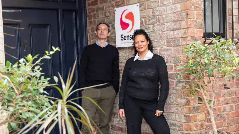 Two Sense colleagues standing beside the Sense sign outside the office