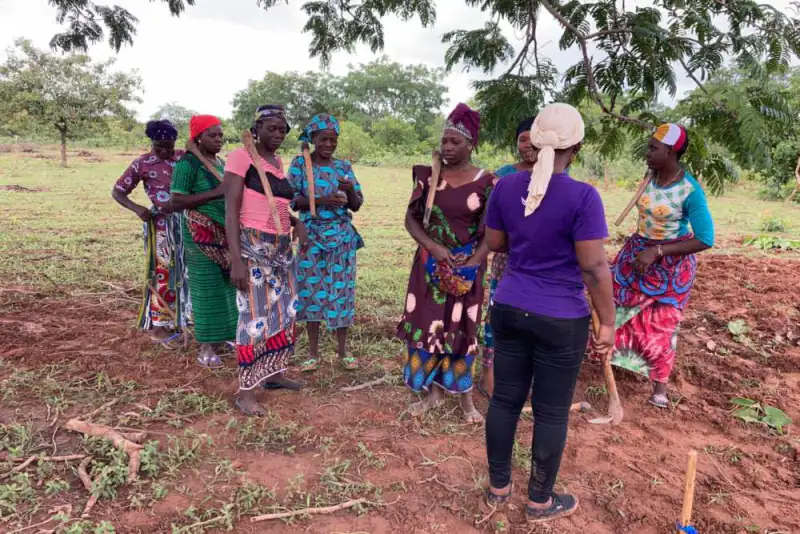 Women farmers with hoes talk with a facilitator in a field, Burkina Faso