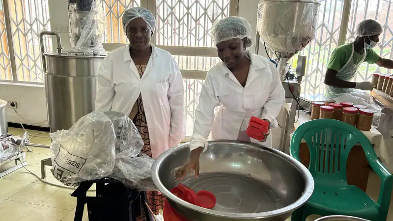 Two women in hairnets and white coats at work in a small food processing room, Malawi
