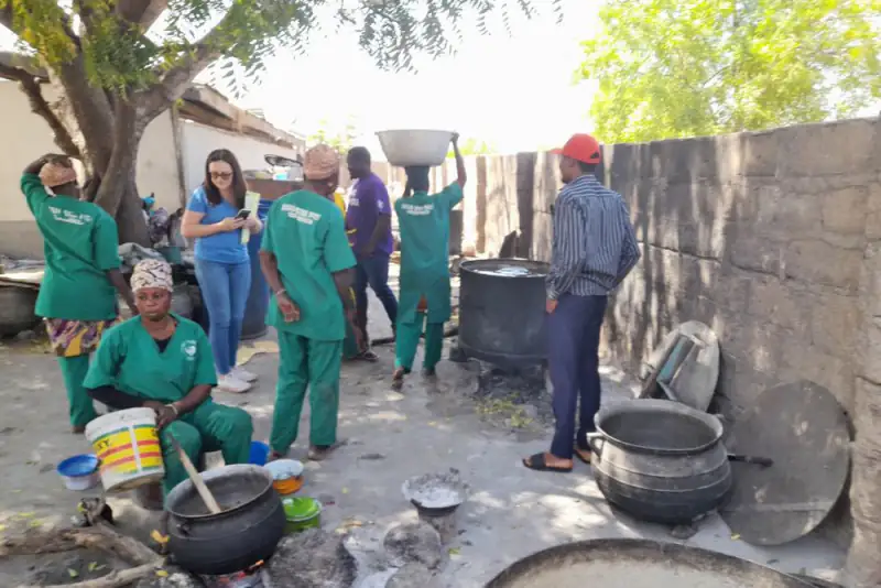 Rice parboilers in green uniforms work at large pots over wood fires